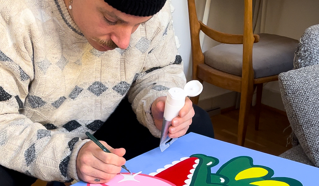Bambi Bakbi painting a colorful crocodile design, using a brush and white paint tube.