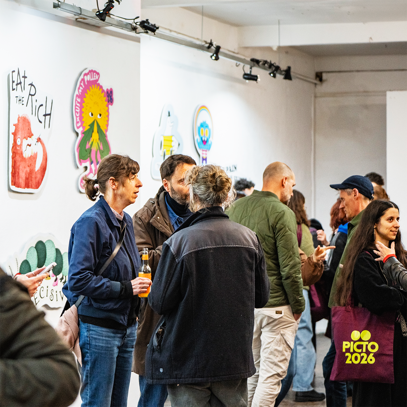 Visitors at an art exhibition talking, behind them artwork made of wall stickers hanging on display.