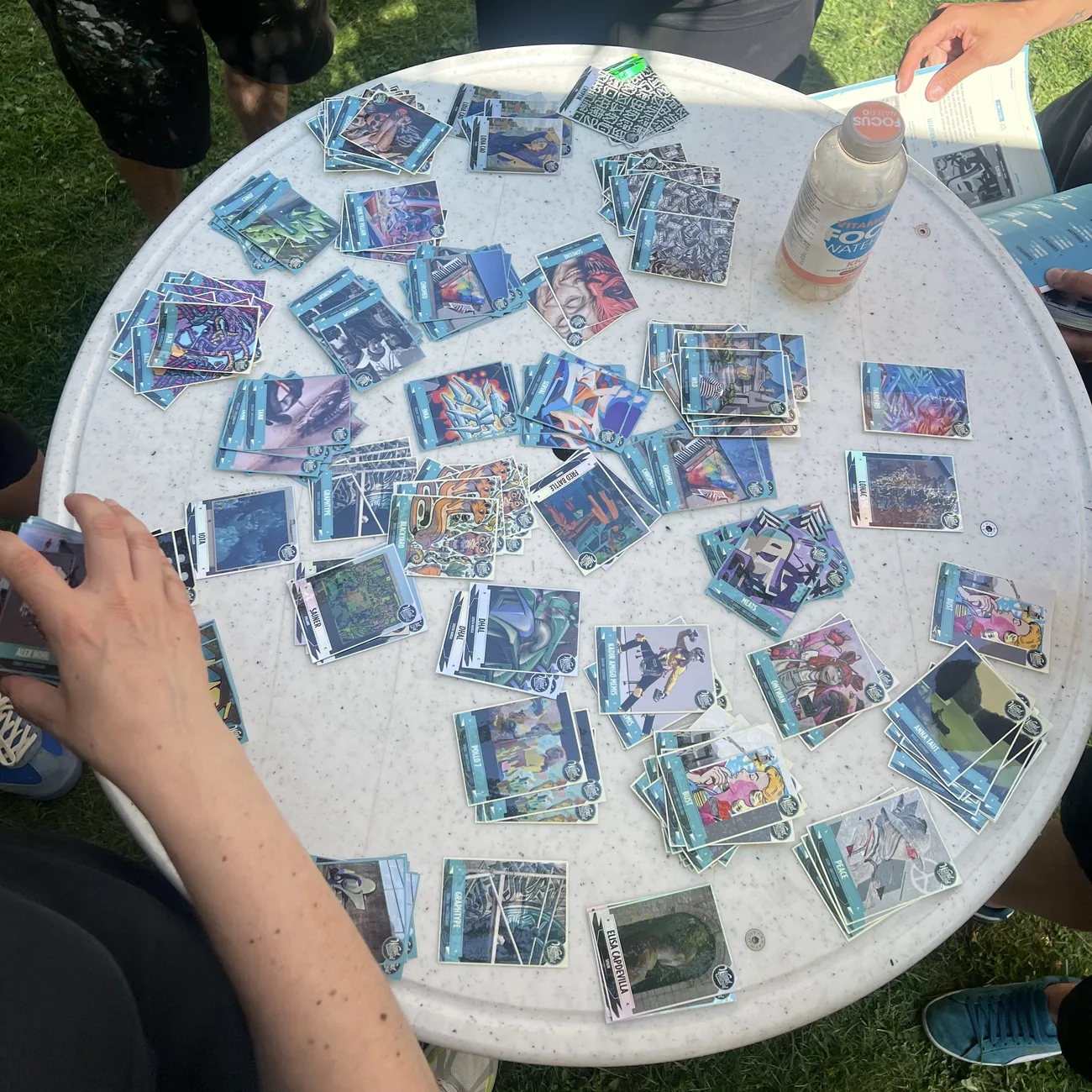 Visitatori del festival riempiono album blu con adesivi da collezione di street art sparsi su un tavolo rotondo