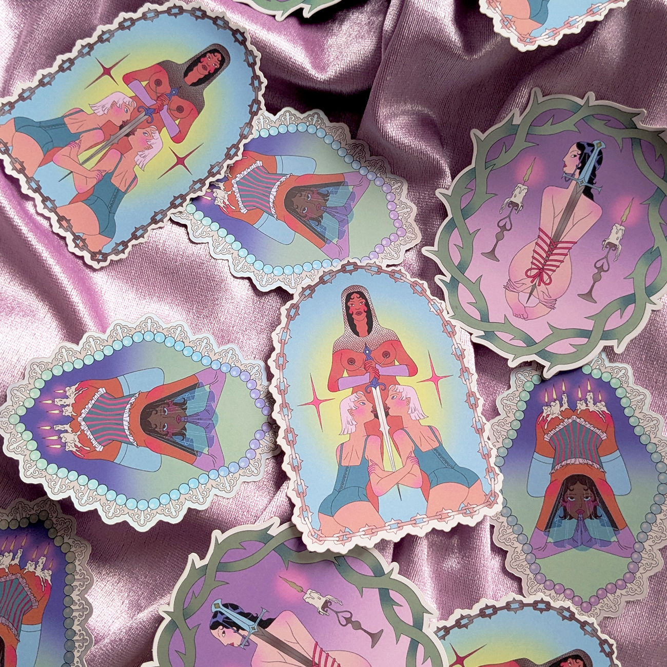 Illustrated die-cut stickers on a silky pink fabric, featuring various women in stylized designs with vibrant colors and ornate borders.