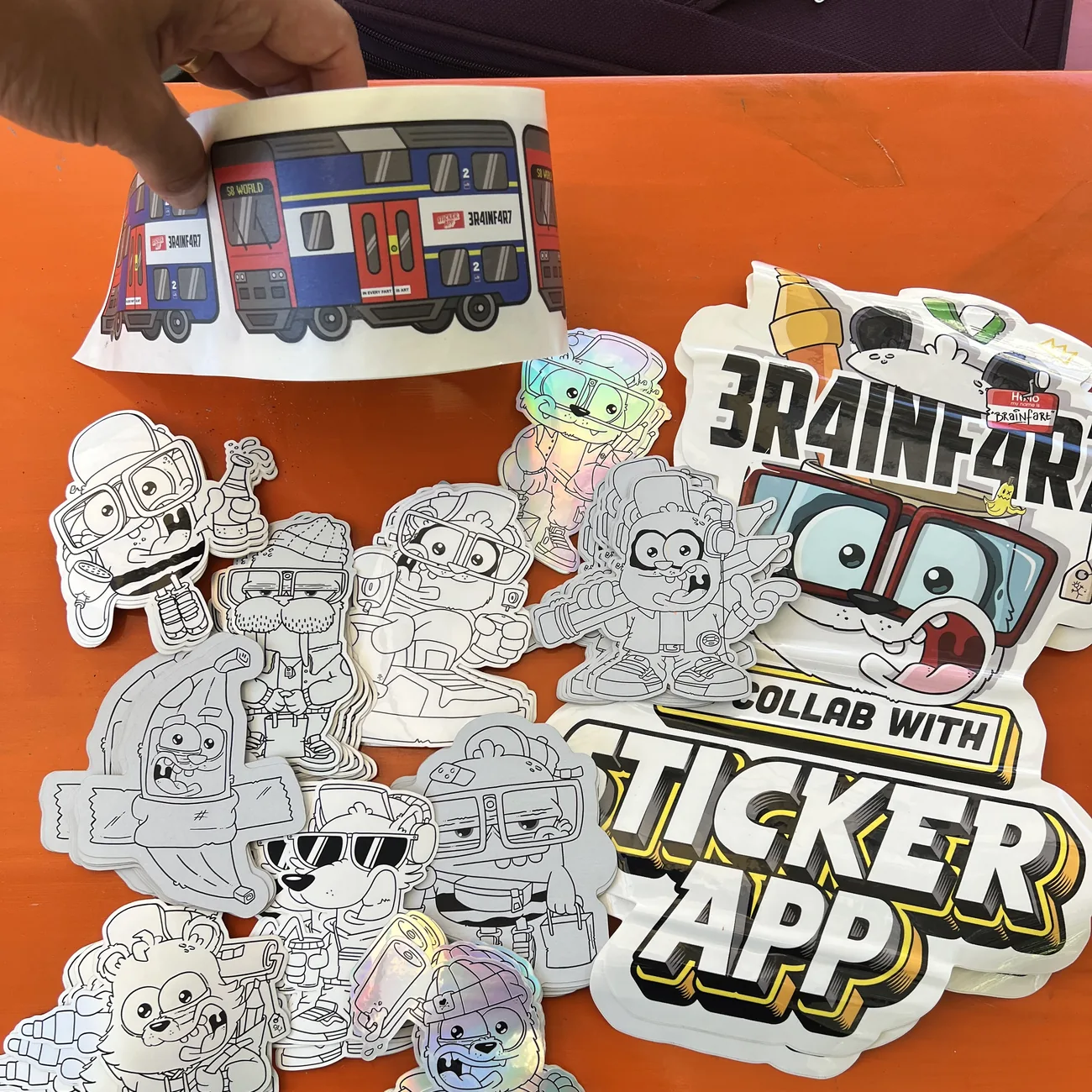 Etichetta del treno S8 World di Brainfart x StickerApp con il cartello "In every fart is art", tenuta sopra adesivi sagomati in bianco e nero