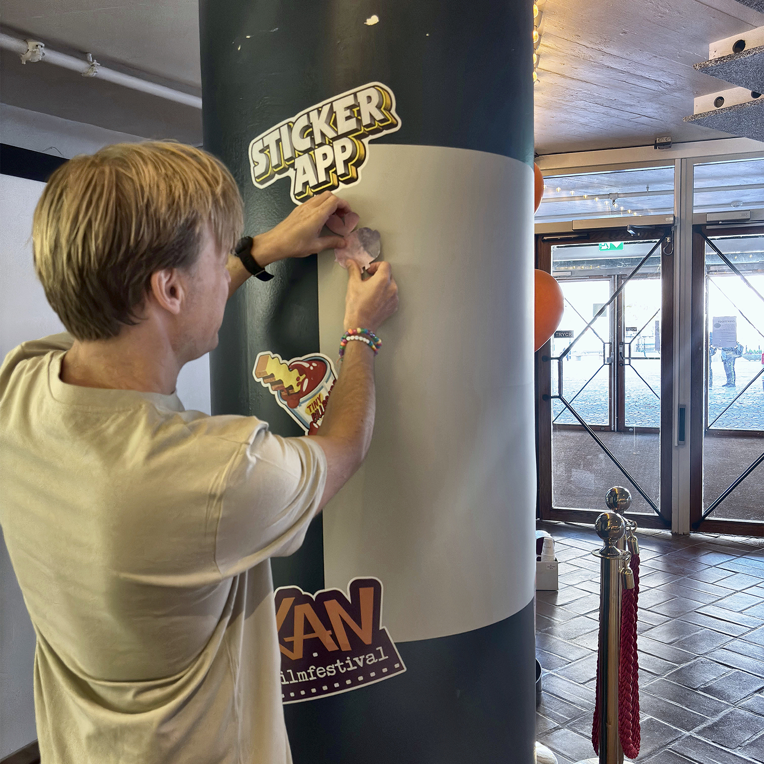 Uomo che attacca un adesivo su un muro di sticker StickerApp avvolto intorno a una colonna al KAN Film Festival
