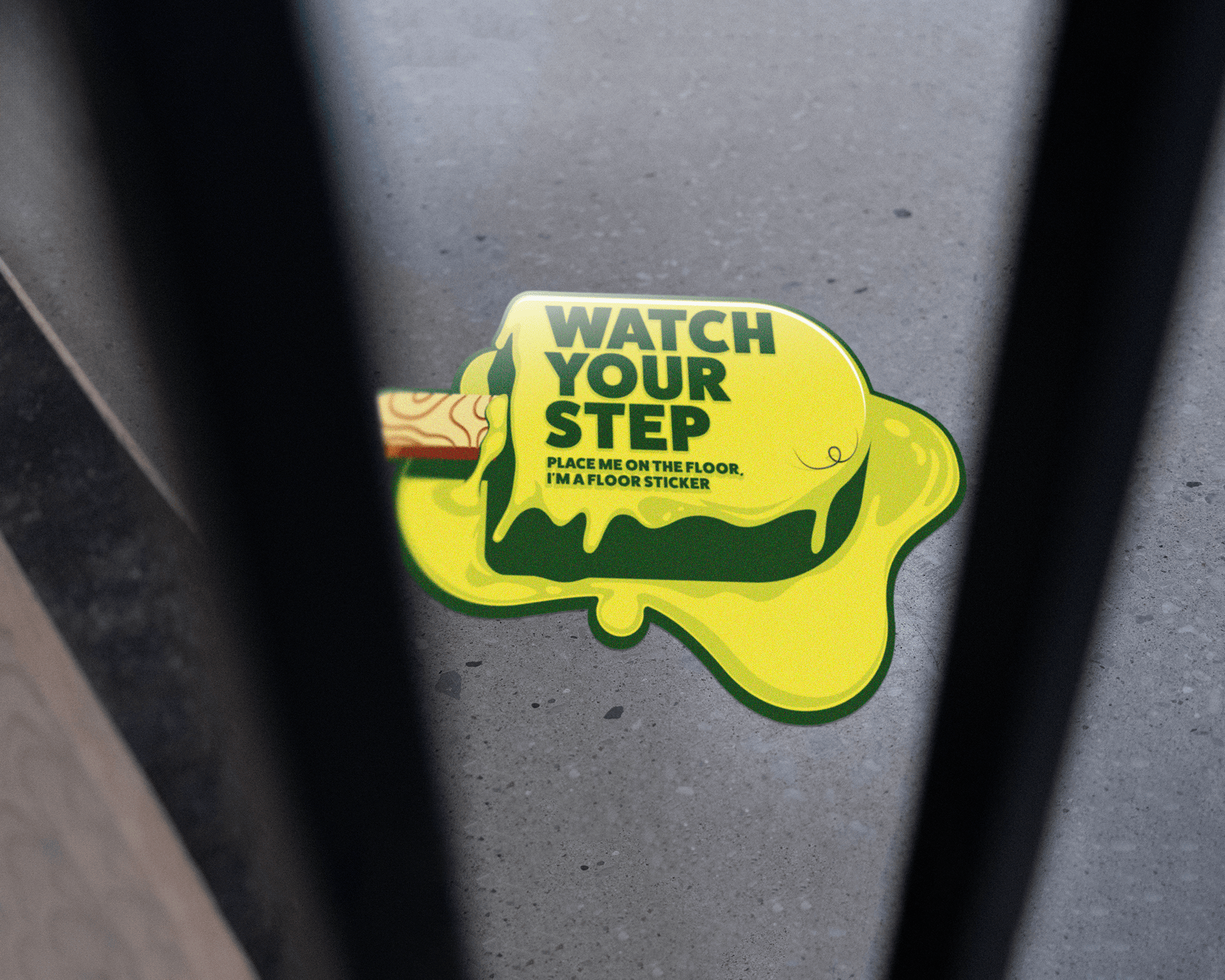 Floor sticker with green slime design and text "WATCH YOUR STEP, PLACE ME ON THE FLOOR. I'M A FLOOR STICKER" on concrete surface.