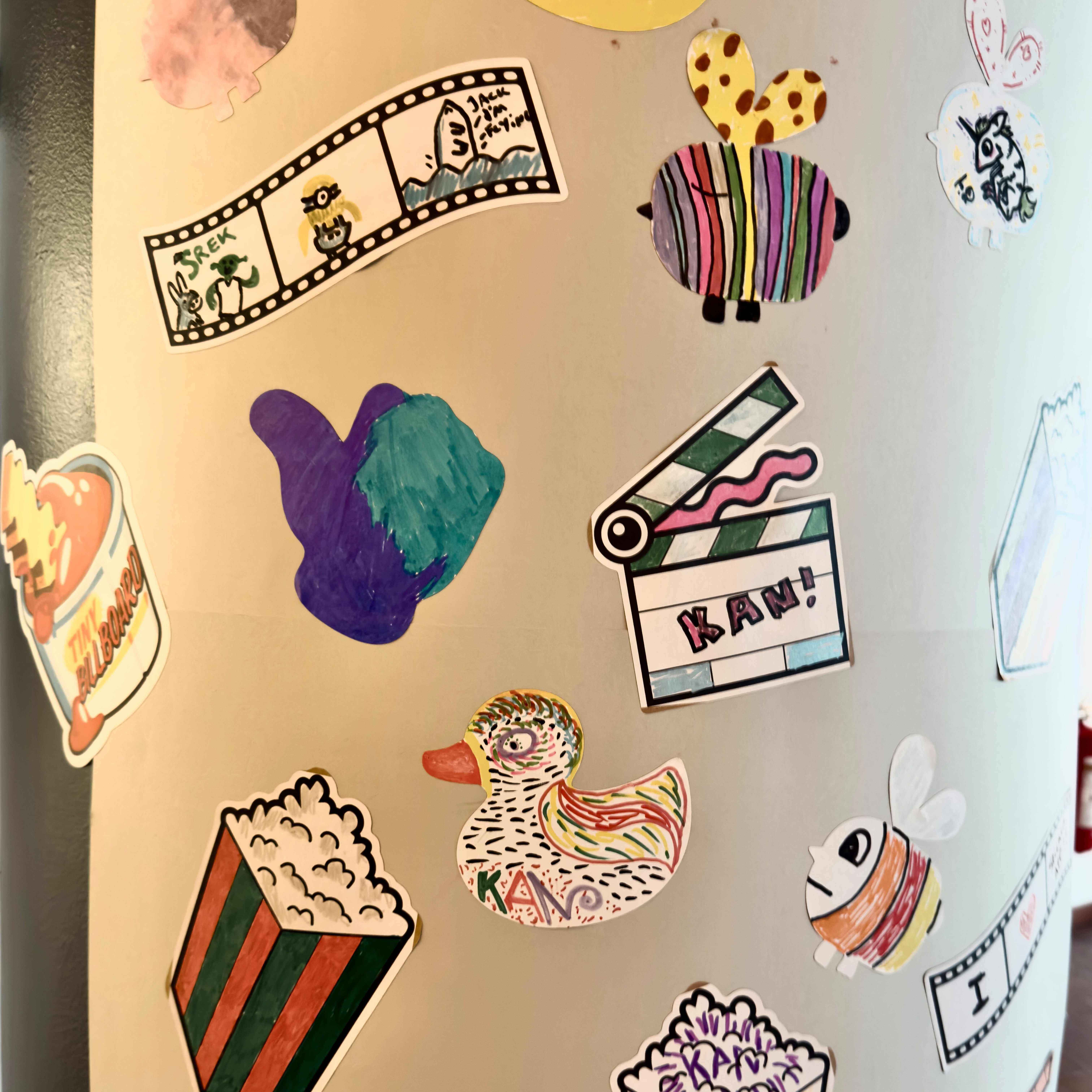Colonna ricoperta di sticker disegnati a mano dai visitatori del KAN Film Festival, tra cui popcorn, pellicole, un'anatra e un ciak con la scritta “KAN!”