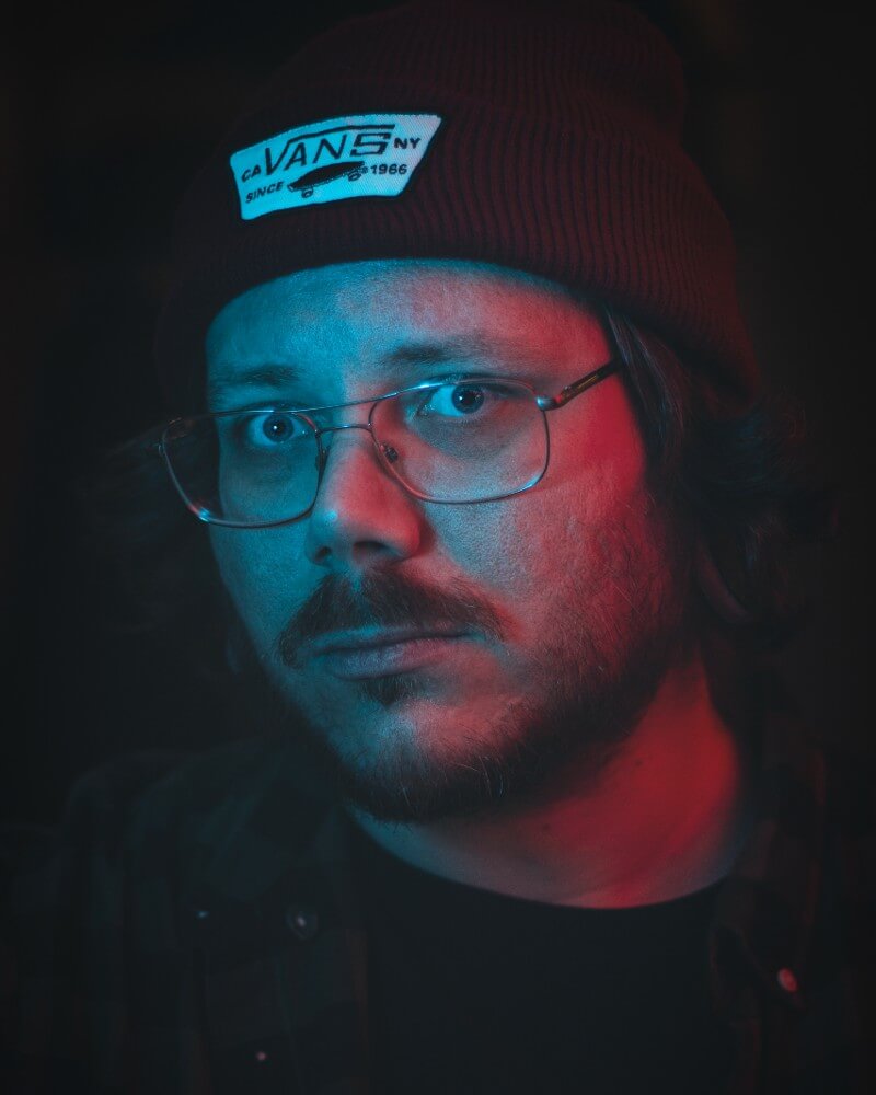 Ritratto dell'artista Emil Ronnelin (Bloodstrokes) con occhiali e berretto sotto luce rossa e blu