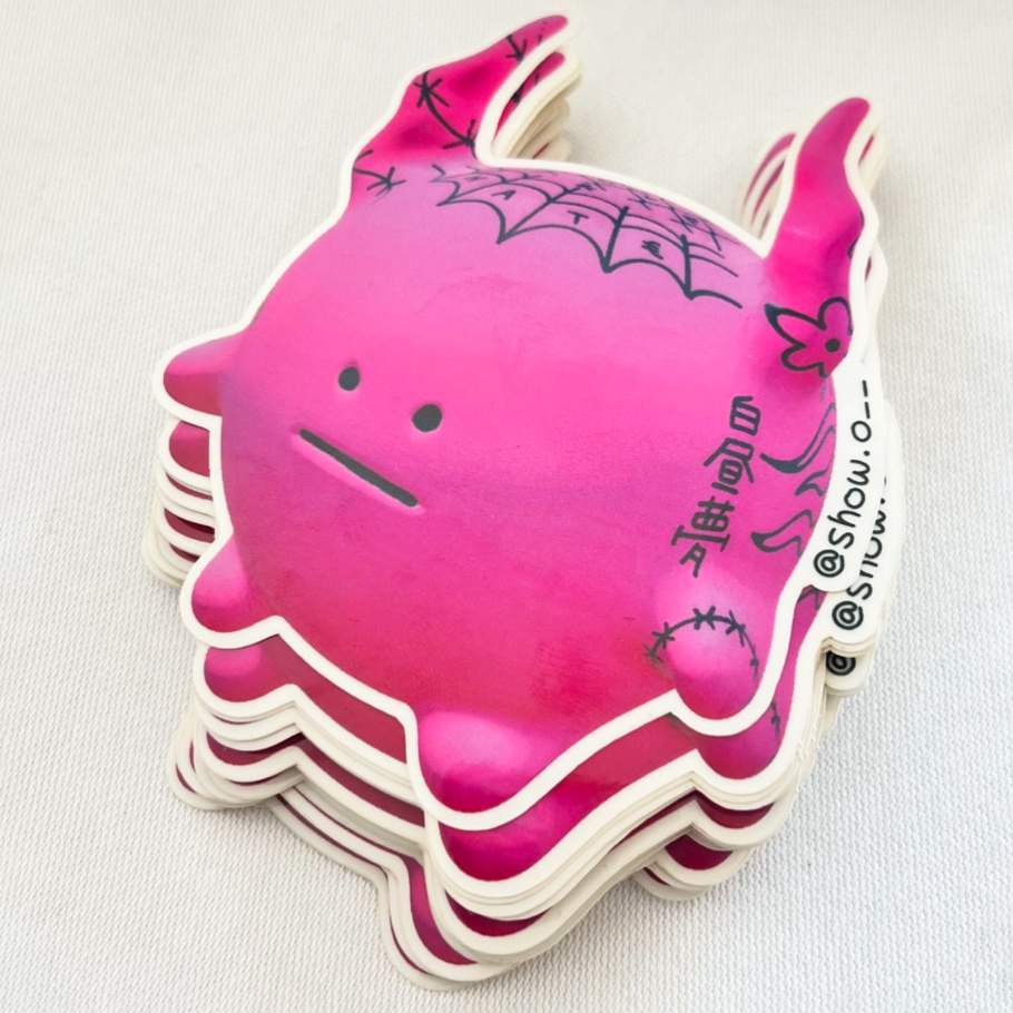 Stack of pink stickers featuring a cute round creature with ears, bat wings, and stitches, set against a light background.